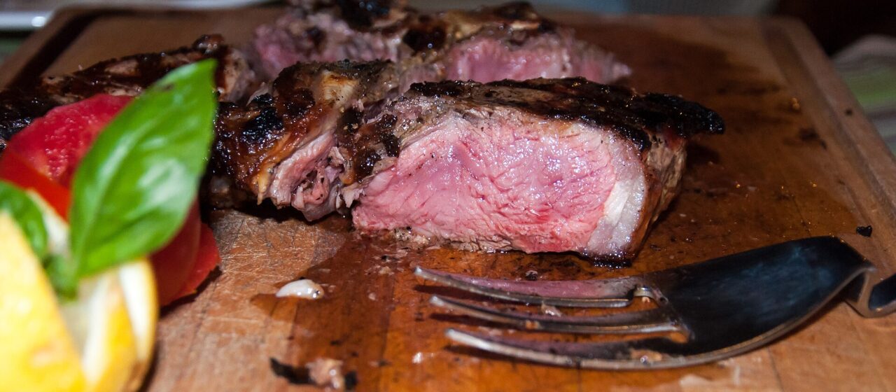 Thick pink-centred bistecca slices rest on a wooden board with cutlery and vegetables at Le Vigne in Radda in Chianti.