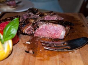 Thick pink-centred bistecca slices rest on a wooden board with cutlery and vegetables at Le Vigne in Radda in Chianti.