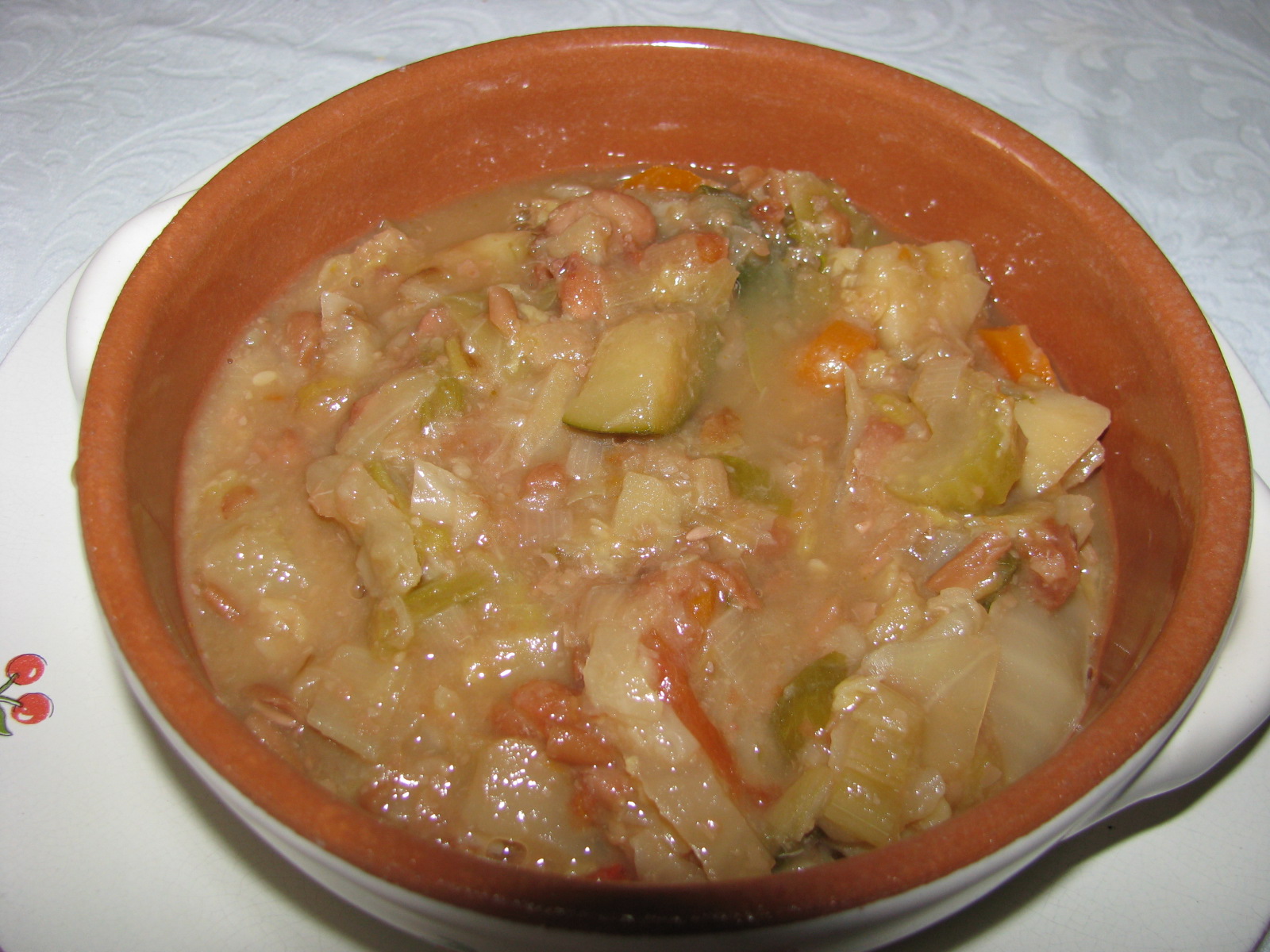 Thick Tuscan ribollita with chunks of vegetables fills a terracotta bowl on a white plate.
