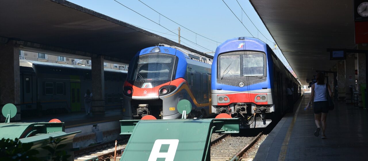 Two regional trains stand beside covered platforms at Florence Santa Maria Novella, with buffers at the track ends.