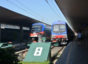 Two regional trains stand beside covered platforms at Florence Santa Maria Novella, with buffers at the track ends.