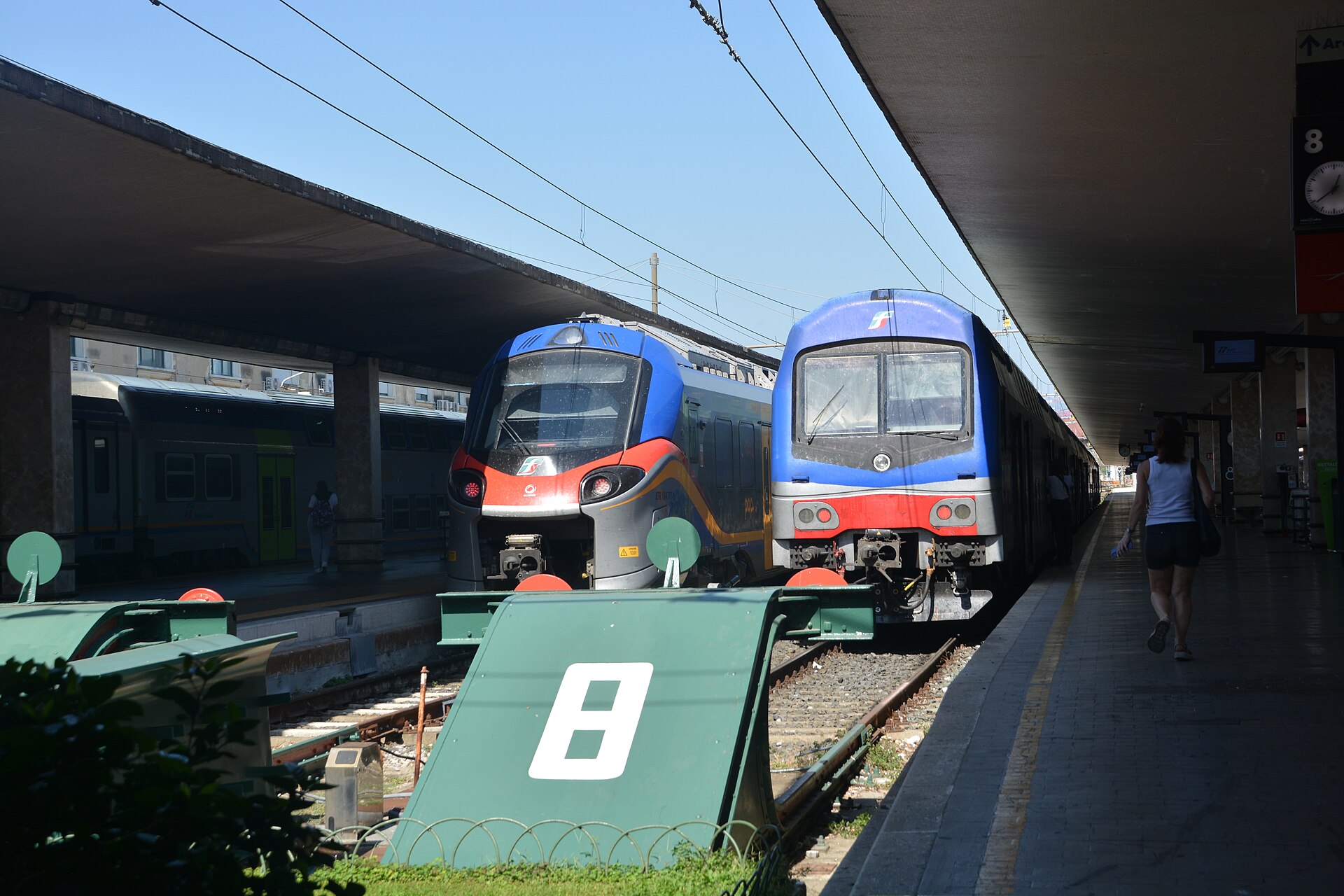 Two regional trains stand beside covered platforms at Florence Santa Maria Novella, with buffers at the track ends.