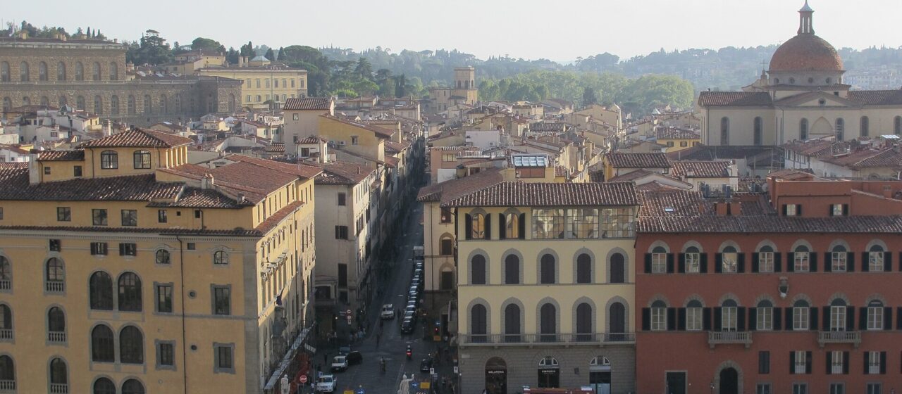 Via Maggio extends into Florence’s Oltrarno beyond Ponte Santa Trinita, surrounded by tiled rooftops and Santo Spirito’s dome.
