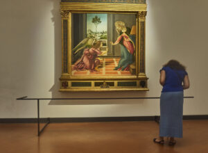A visitor stands before an Annunciation painting in an ornate gilded frame at the Uffizi Gallery in Florence.