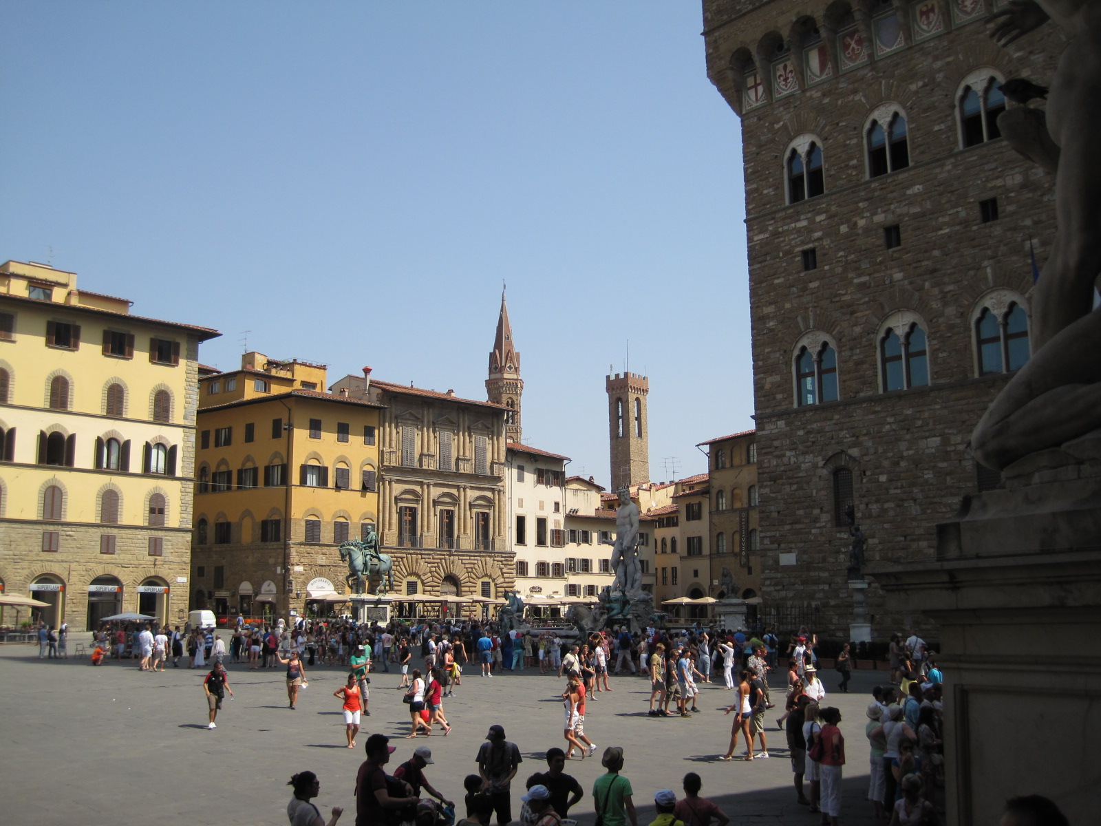 Visitors cross Florence’s Piazza della Signoria and gather beside the Neptune fountain, while others rest in Palazzo Vecchio’s shade.
