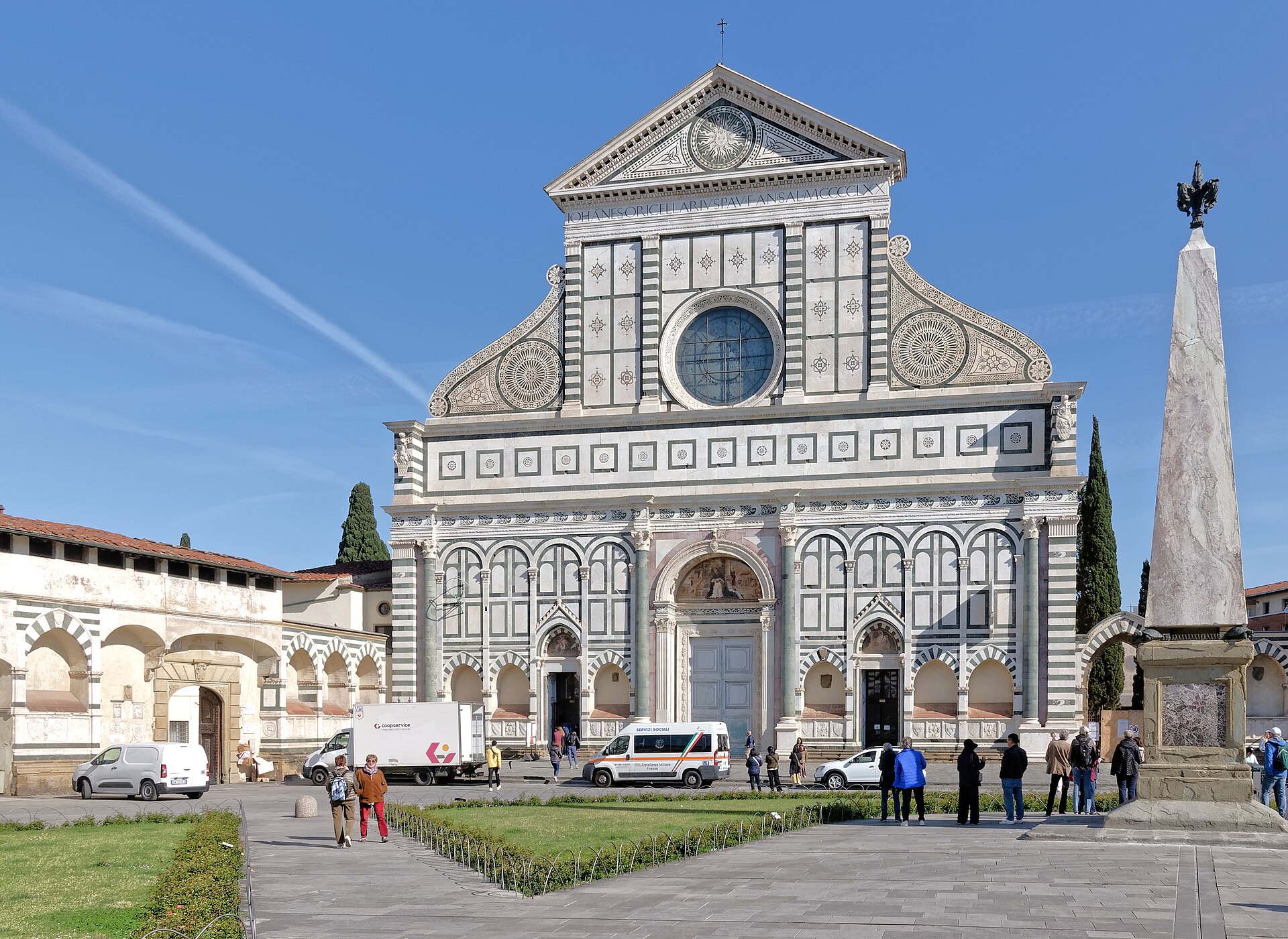 Visitors cross the square before Santa Maria Novella in Florence, with marble scrolls, a round window and an obelisk.