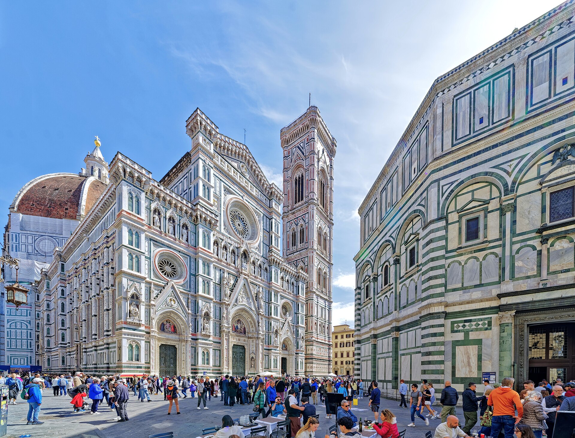 Visitors cross the square beside Florence Cathedral, its patterned marble facade and Giotto's bell tower rising behind the Baptistery.