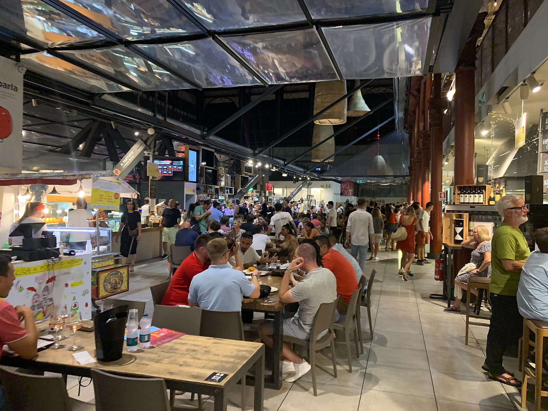 Visitors eat at long wooden tables between food counters and iron columns in Florence's Mercato Centrale upstairs dining hall.