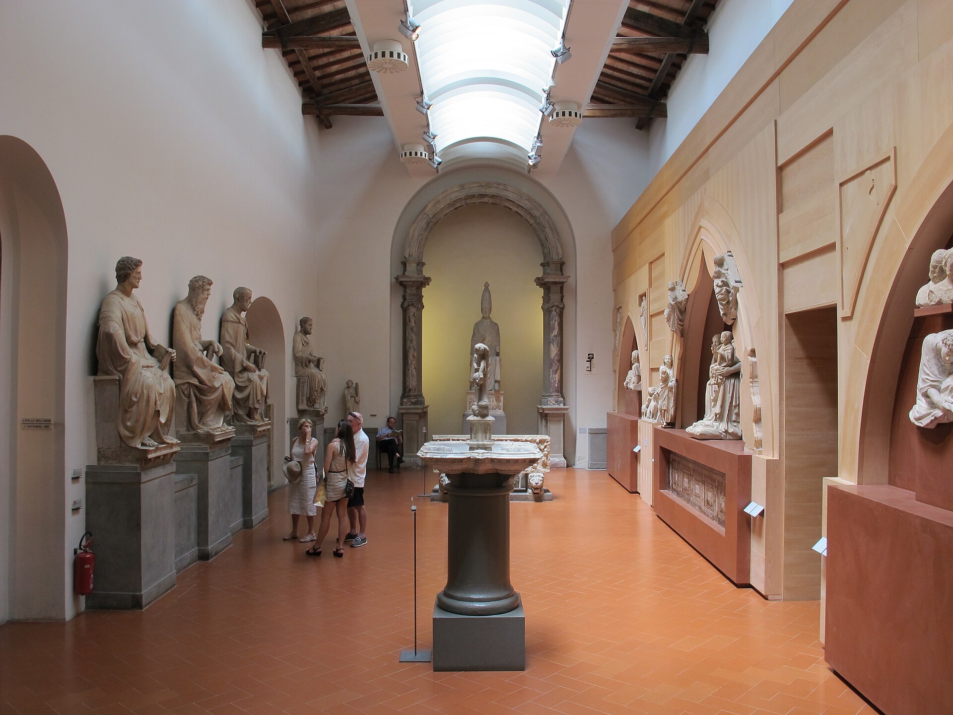 Visitors examine marble sculptures beneath a skylight in Florence’s Museo dell’Opera del Duomo, with statues lining both sides.