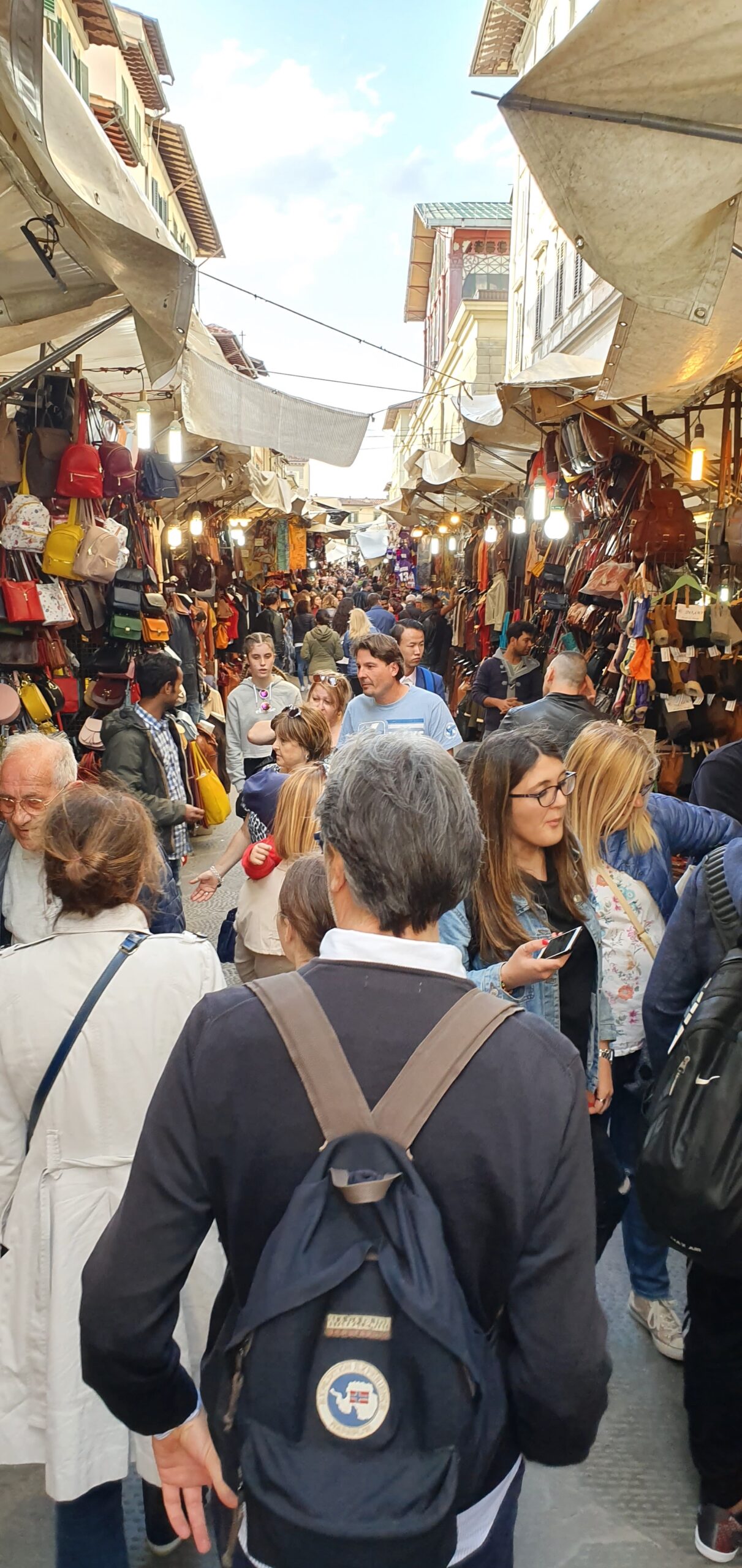 Visitors fill the narrow passage between handbag stalls and awnings at Florence's outdoor San Lorenzo market.