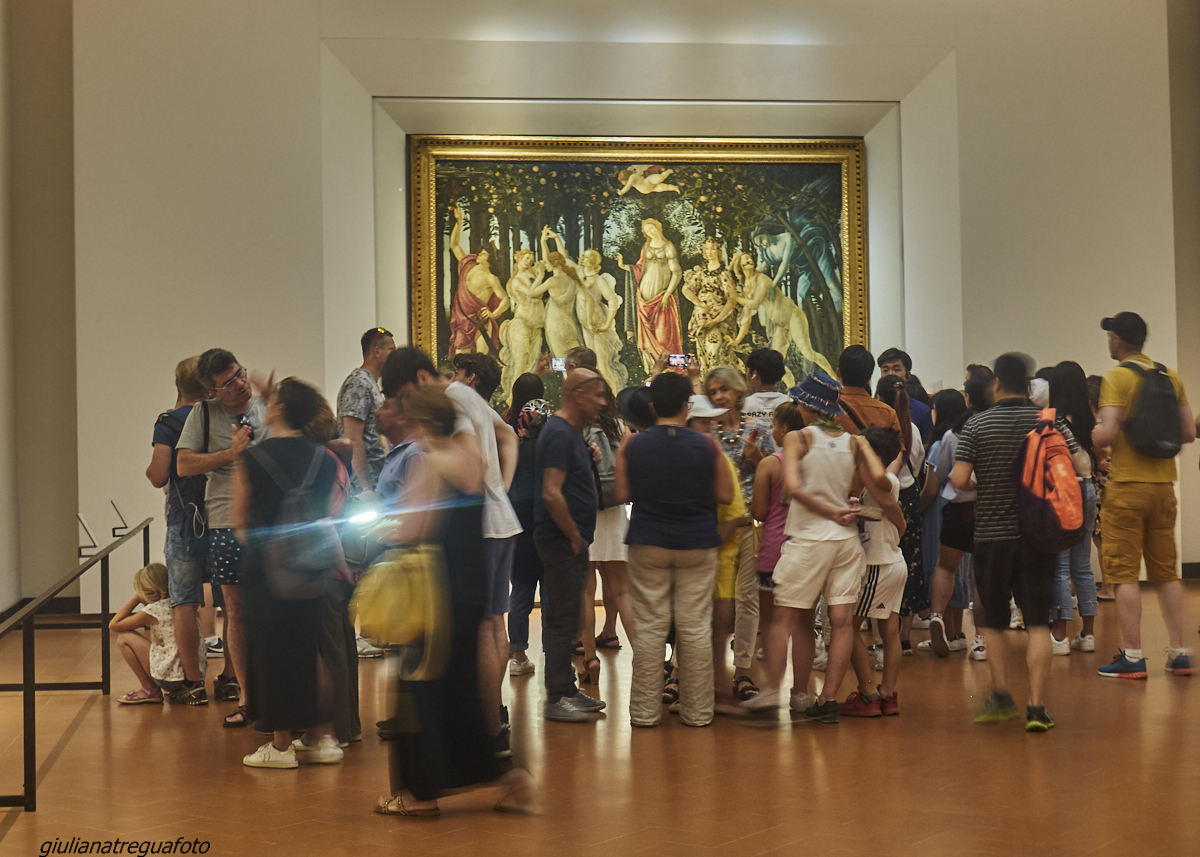 Visitors gather beneath Botticelli's Primavera in its gilded frame inside the Uffizi Gallery's painting rooms in Florence.