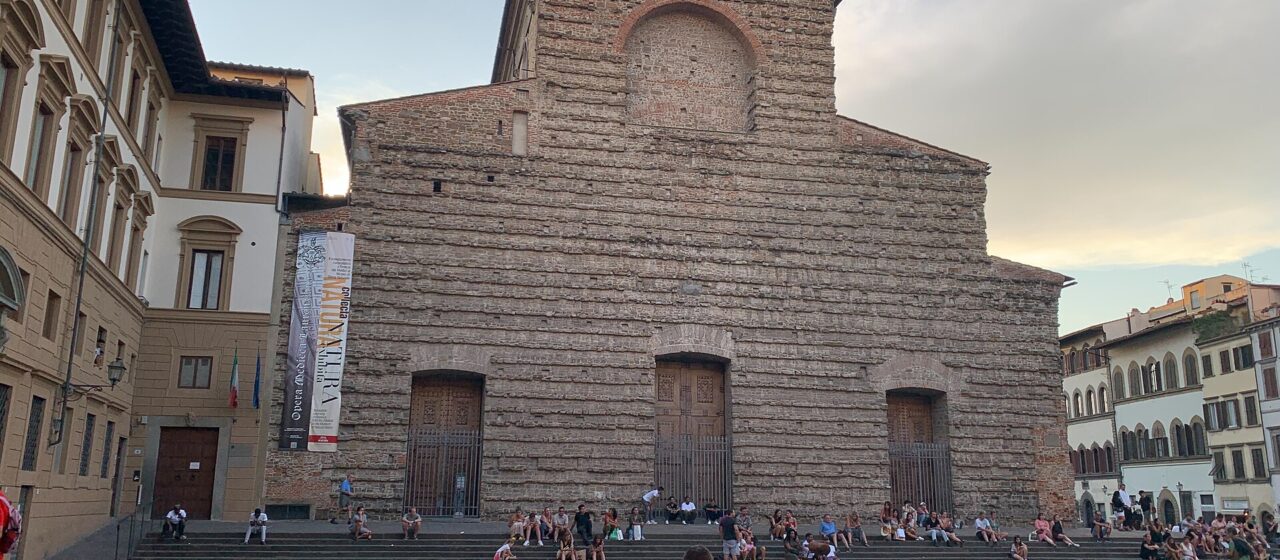Visitors gather on the steps and at outdoor tables before the unfinished facade of San Lorenzo in Florence.