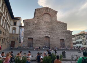Visitors gather on the steps and at outdoor tables before the unfinished facade of San Lorenzo in Florence.
