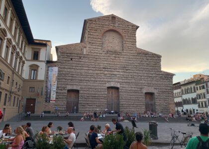 Visitors gather on the steps and at outdoor tables before the unfinished facade of San Lorenzo in Florence.