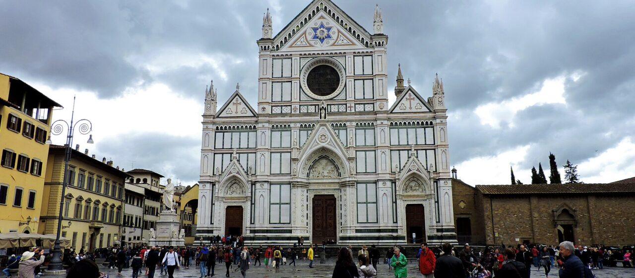 Visitors in jackets and long trousers gather by Santa Croce’s entrance steps and cross the wet piazza in Florence.