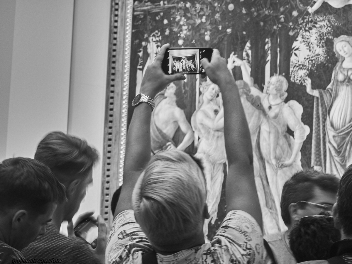 Visitors photograph the Three Graces in Botticelli's Primavera, displayed in a gilded frame at the Uffizi Gallery in Florence.