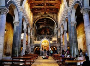 Visitors stand among stone columns beneath striped arches and a timber roof inside Florence's San Miniato al Monte.