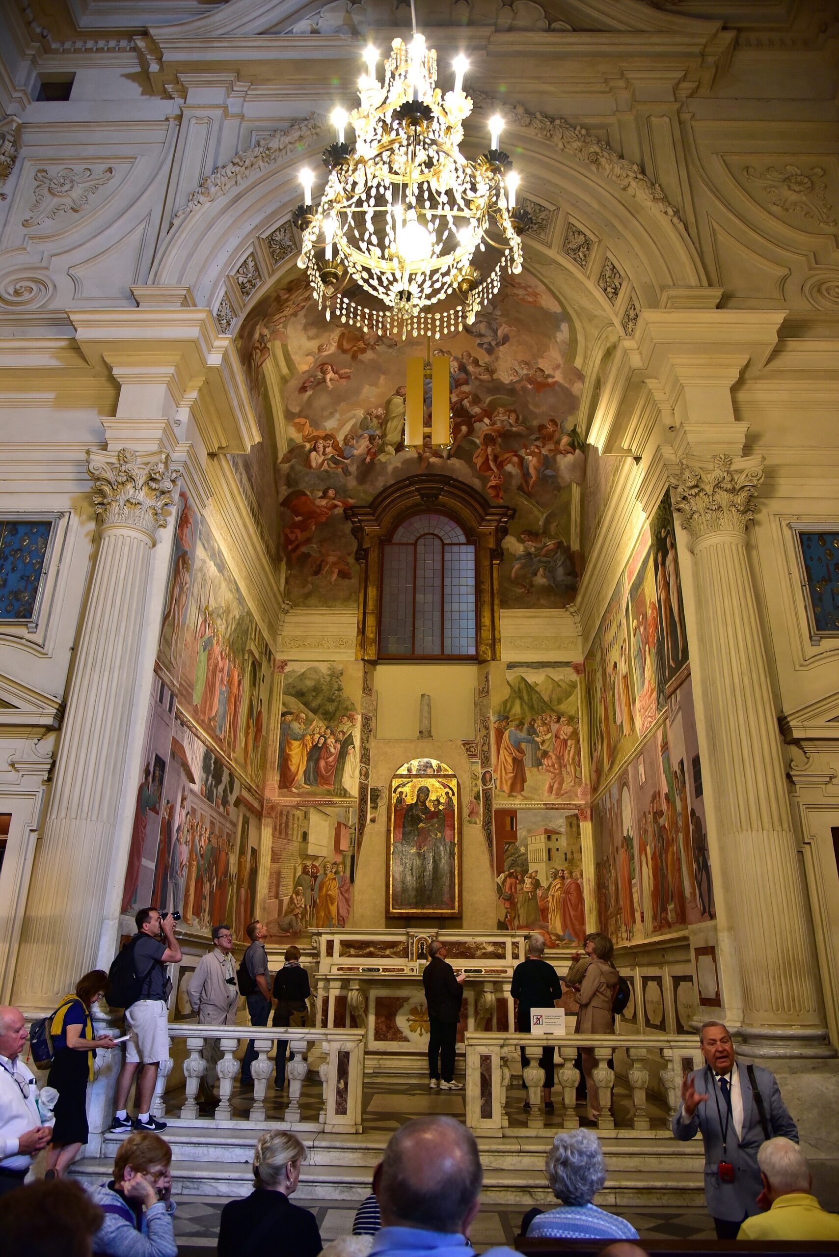 Visitors stand before the altar and fresco-covered walls of the Brancacci Chapel in Santa Maria del Carmine, Florence.