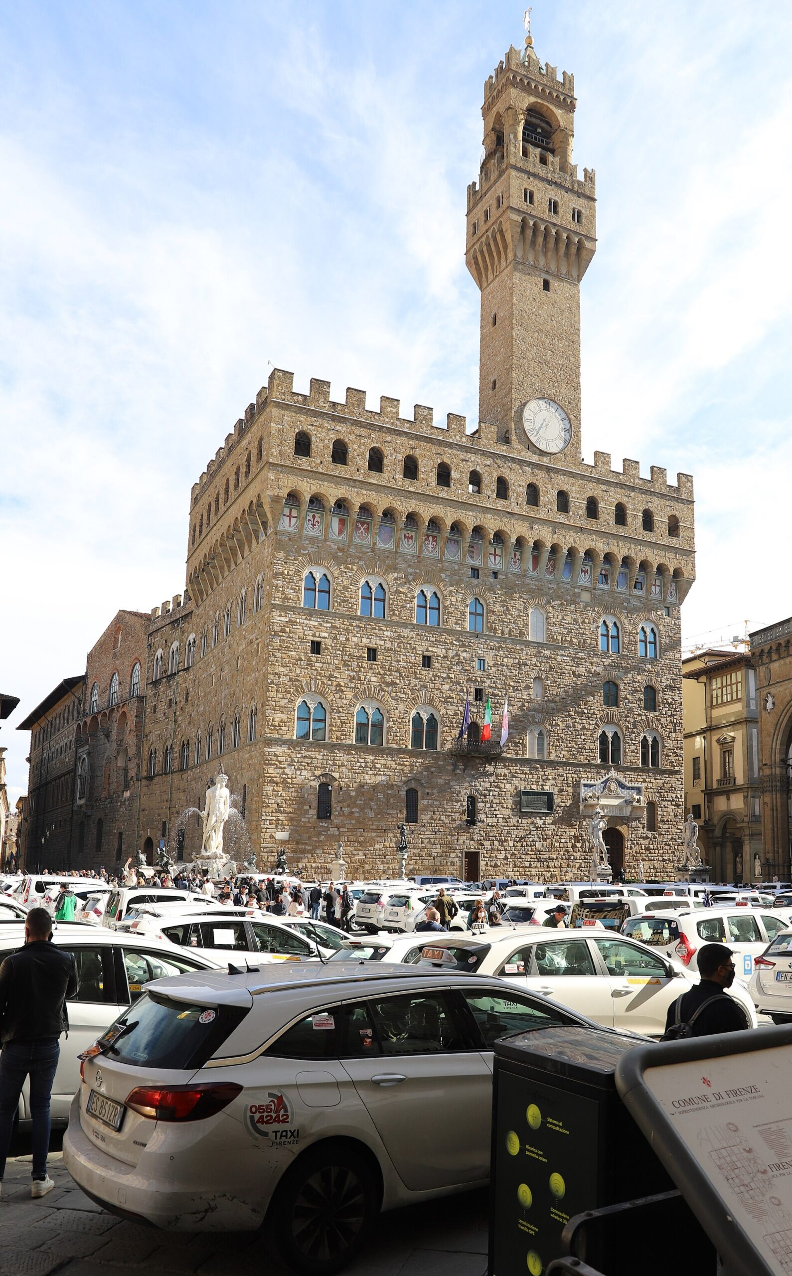 White Florence taxis with roof signs and door identifiers gather in Piazza della Signoria below Palazzo Vecchio’s tower.