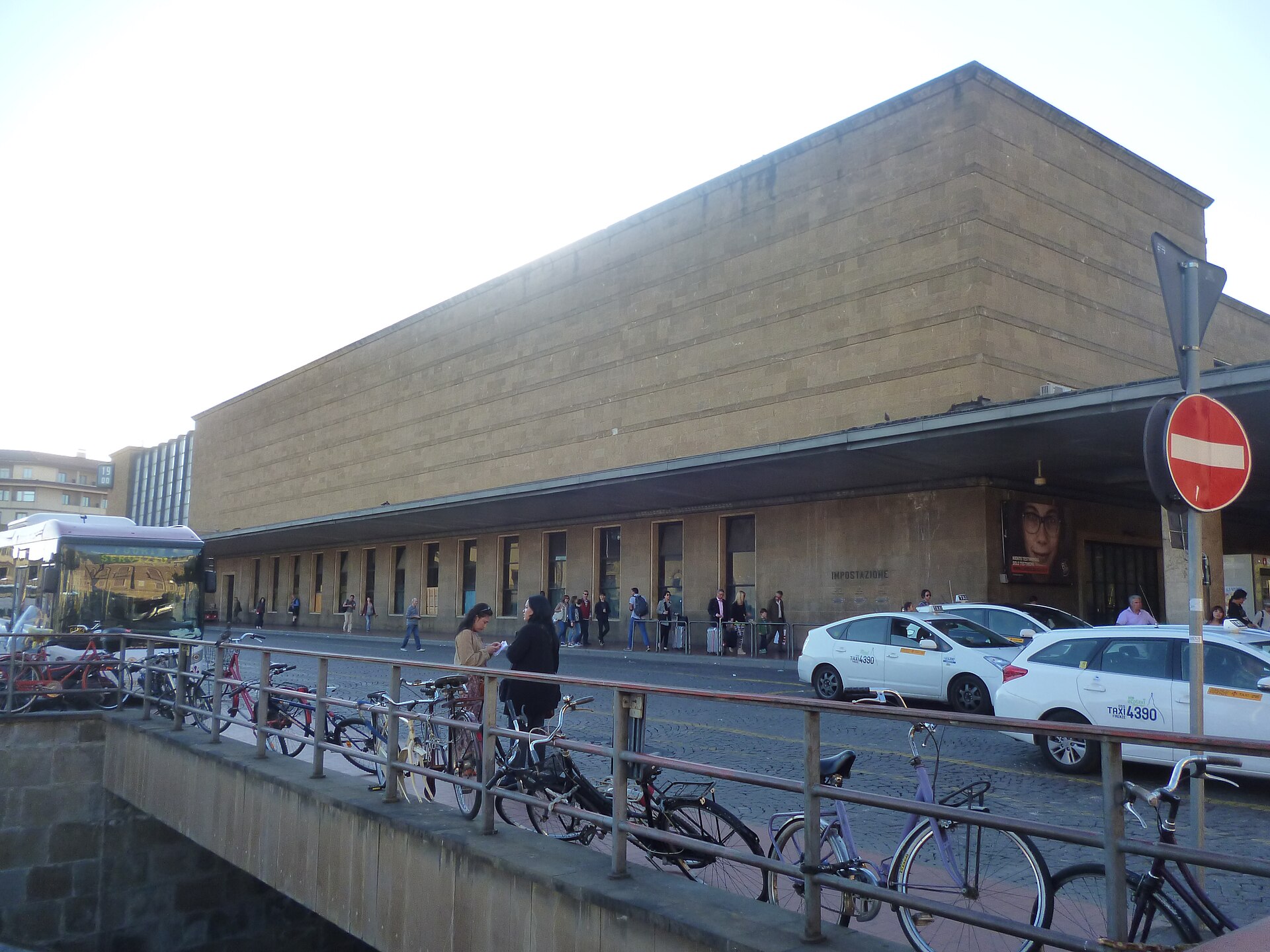 White Florence taxis wait beside Santa Maria Novella station, behind railings lined with parked bicycles.