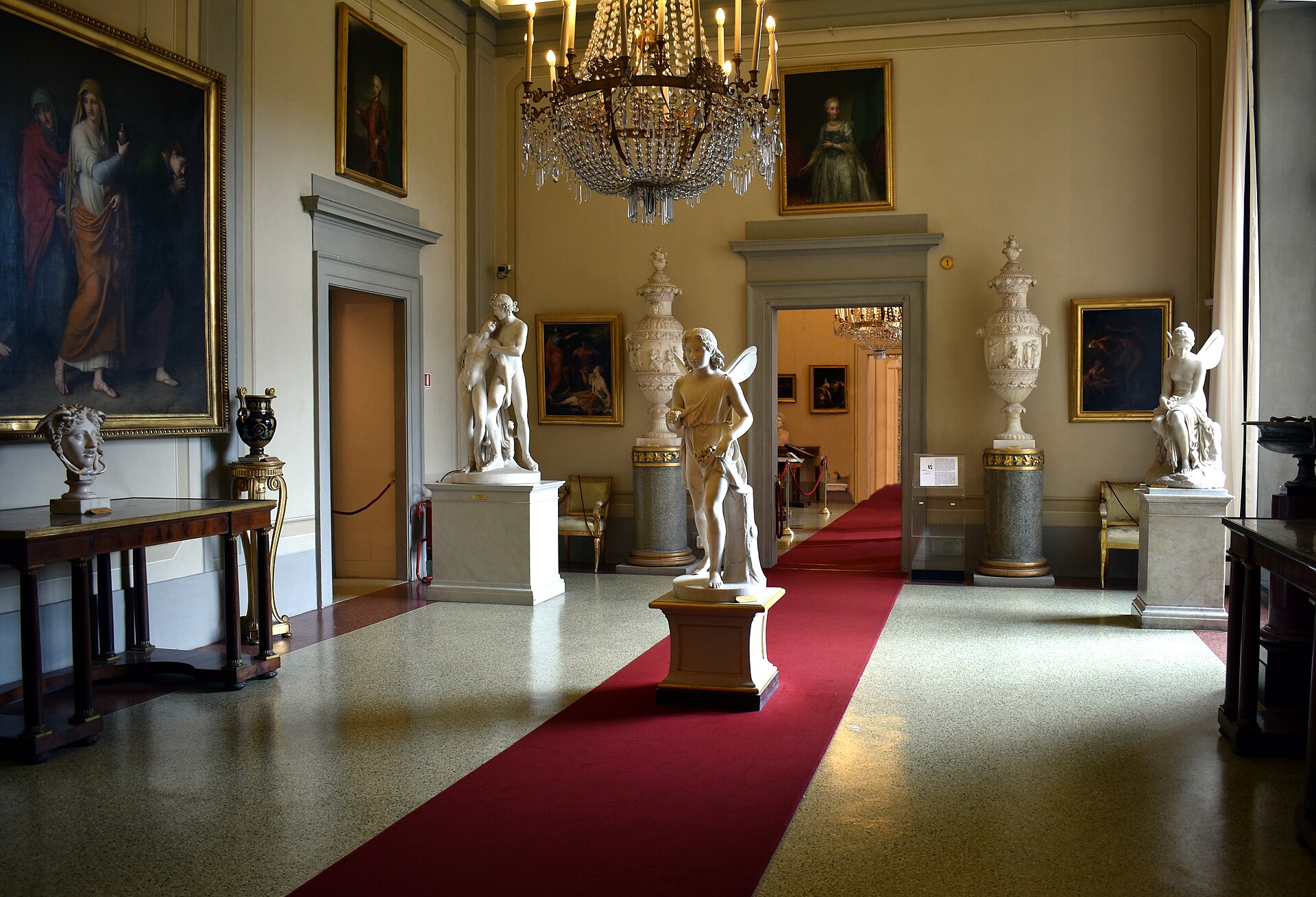 White marble statues, framed paintings and a chandelier fill a room of the Modern Art Gallery at Palazzo Pitti in Florence.